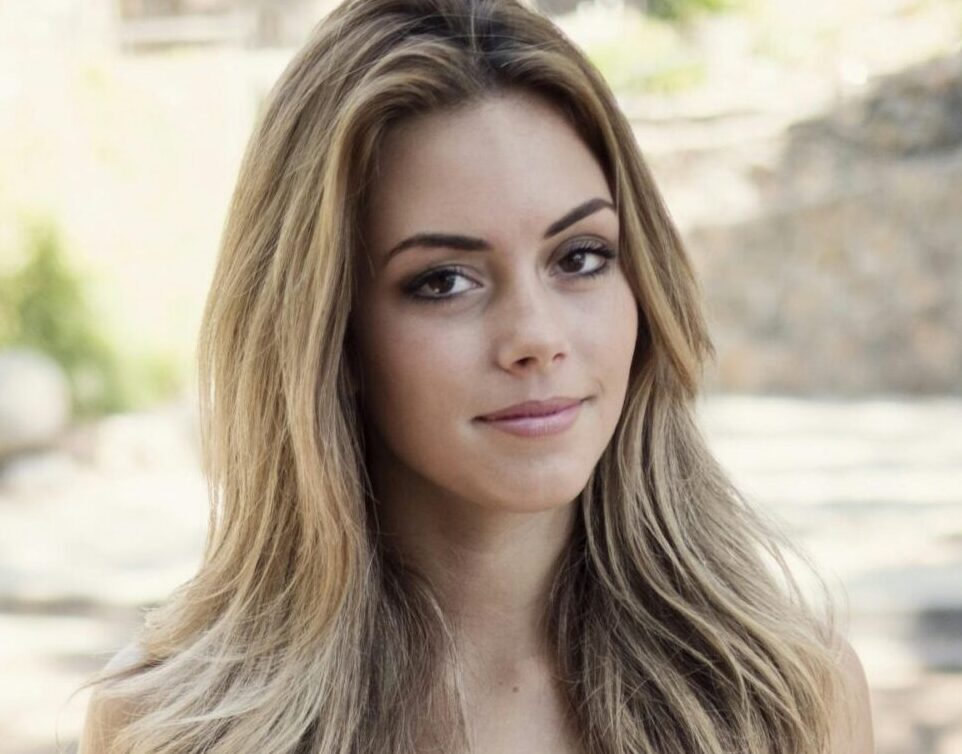 Portrait of a young woman in a white dress sitting outdoors on a sunny day.